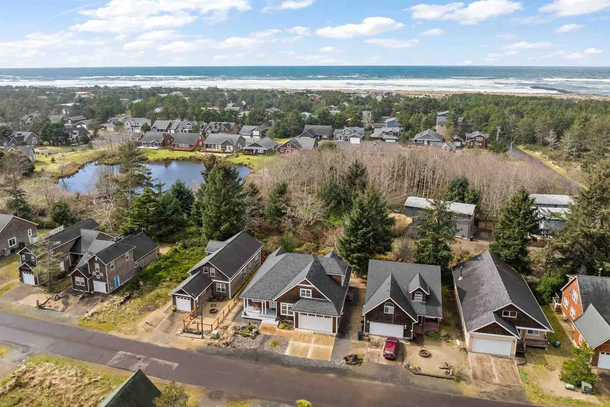 A relaxed, panoramic view of the ocean with a glimpse of the neighborhood, pond, and green trees. Houses are scattered throughout, suggesting a friendly community close to nature, with opportunities for walking and exploring.