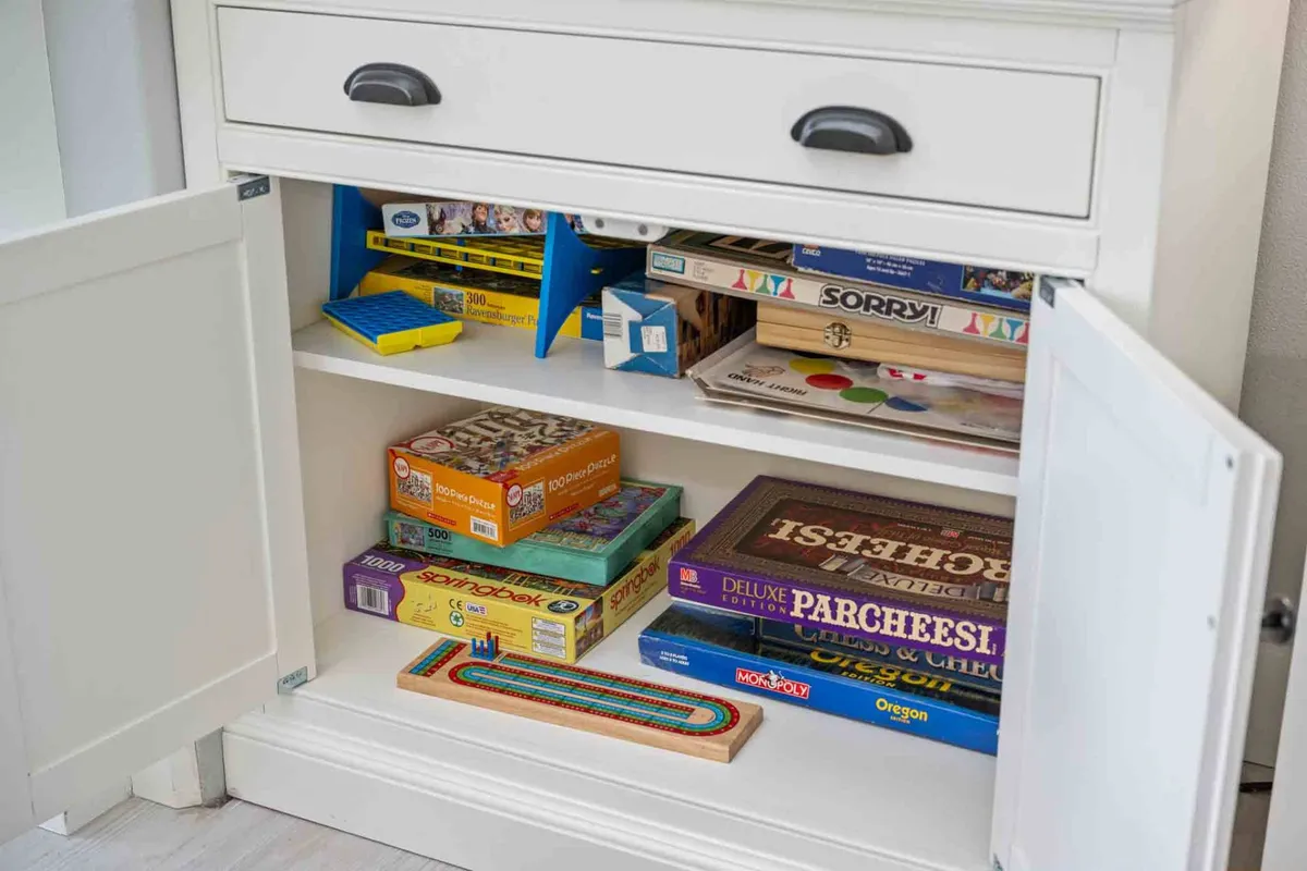 A bright, playful interior scene with a cabinet of colorful board games ready for family fun and friendly competition. The mood is nostalgic and lively, reflecting the spirit of game nights and shared memories.