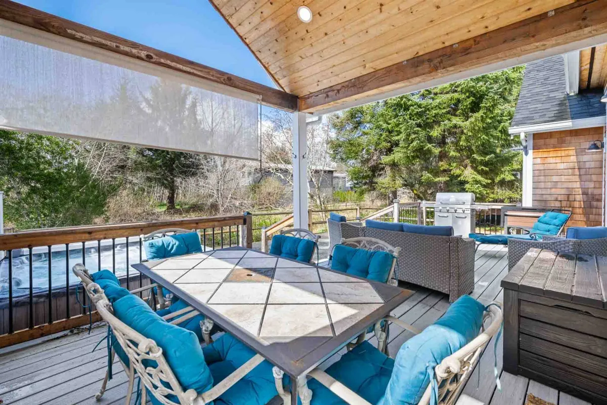 An inviting exterior deck setup with a dining table, lounge seating, grill, and lush greenery. The space suggests relaxation, outdoor meals, and enjoying the coastal air, possibly with a pet lounging nearby.