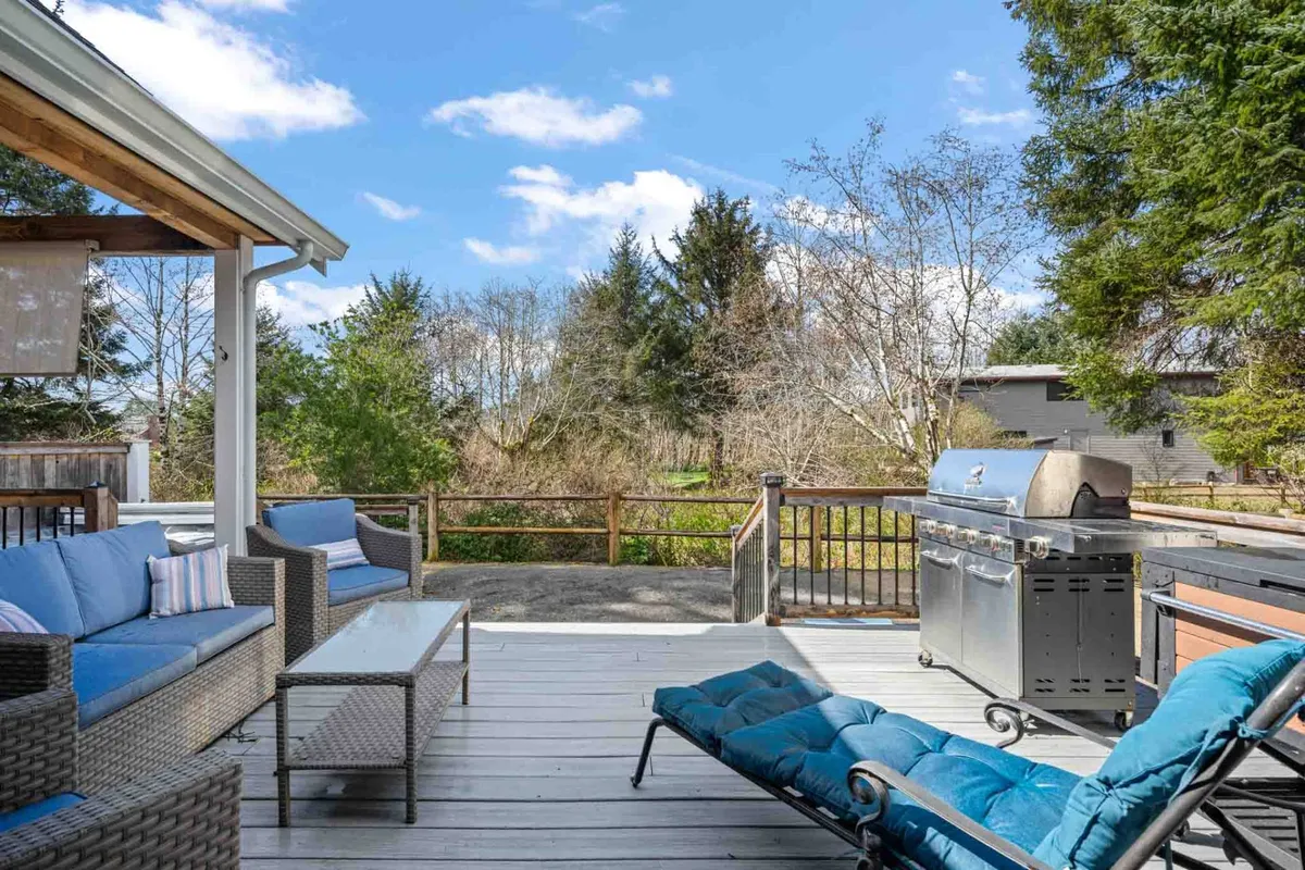 This image showcases an inviting outdoor seating area on a wooden deck, complete with a grill and surrounded by a wooden railing. The space is designed for relaxation and socializing, with comfortable lounge furniture and open sky views that hint at the surrounding natural environment.
