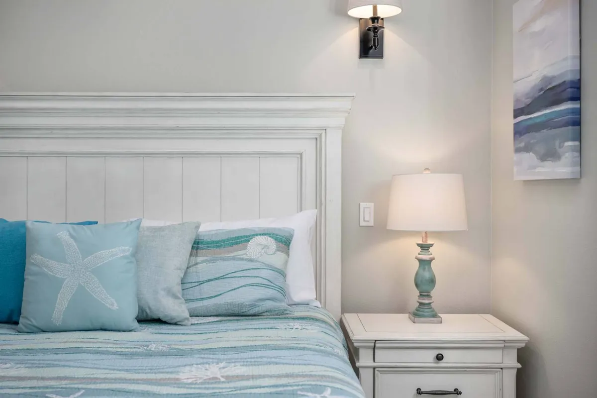 A peaceful bedroom scene showcasing a bed with decorative pillows and a soft throw, a nightstand with a glowing lamp, and subtle wall art. The overall feel is one of comfort and tranquility, suggesting a restful retreat for guests.