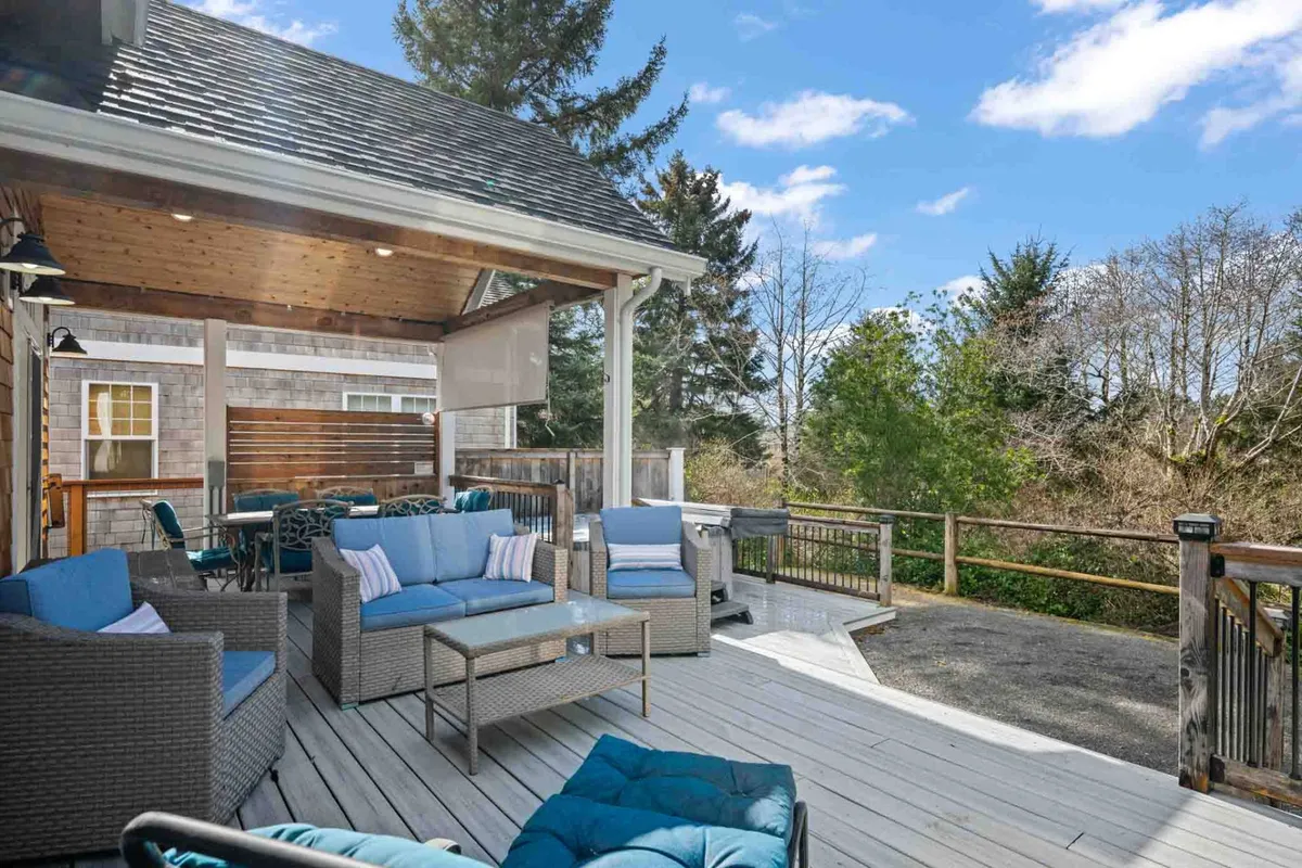 A comfortable outdoor seating area with an inviting grill and wooden railing, nestled among mature coastal pines. The deck promises sunset views and relaxed moments surrounded by lush greenery, offering a perfect spot to unwind after a day of exploration.