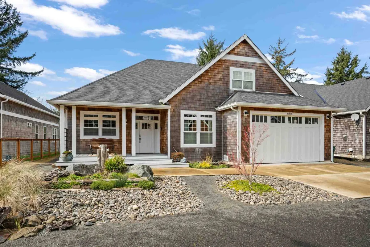 An exterior view featuring the front porch, a gravel pathway, and a landscaped garden. The setting is tranquil and welcoming, suggesting easy access to outdoor adventures and a harmonious relationship with the natural surroundings.