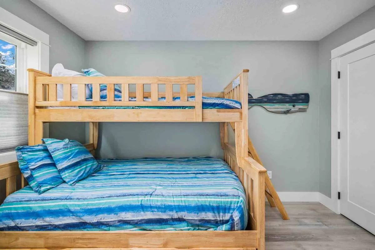 A playful bunk room with striped bedding on bunk beds and whimsical decorative whale art above. The room balances fun and coziness, offering a comfortable space ideal for kids to relax, play, or read before bedtime.